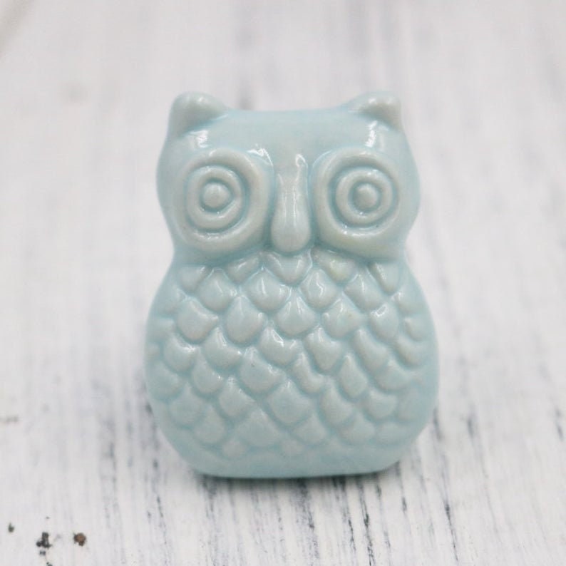 May include: A light blue ceramic owl figurine with a textured, scaly design. The owl has large, round eyes and a small beak.