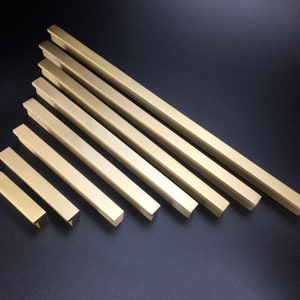 May include: A set of eight gold-toned metal cabinet pulls in various sizes. The pulls are rectangular in shape with a slightly rounded edge.