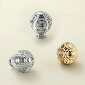 Peut inclure: Trois boutons ronds pour armoire avec un design strié. Les boutons sont en finition argent, or et chrome.