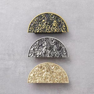 May include: Three half-round cabinet knobs with a floral design. The knobs are in gold, silver, and black.
