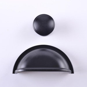 May include: Two black cabinet knobs. One is a round knob and the other is a half-round, arched knob.