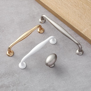 May include: Four cabinet pulls in different finishes: gold, white, and two silver. The silver pulls are a long handle and a round knob.