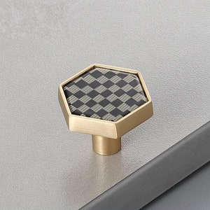 Pu&ograve; includere: Un pomello per cassetti esagonale con finitura dorata e un motivo a scacchi bianco e nero.