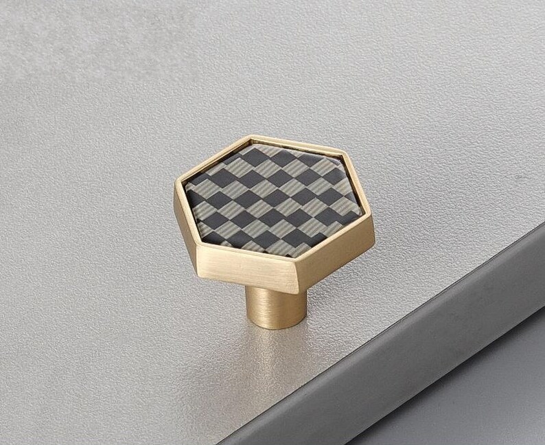 Pu&ograve; includere: Un pomello per cassetti esagonale con finitura dorata e un motivo a scacchi bianco e nero.