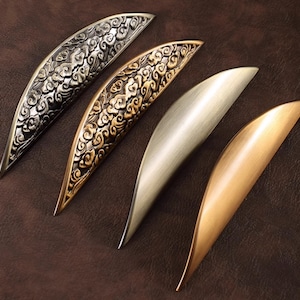 May include: Four decorative cabinet pulls in different finishes. Two pulls feature a detailed cloud design in a gold and silver finish. The other two pulls are smooth and feature a silver and copper finish.