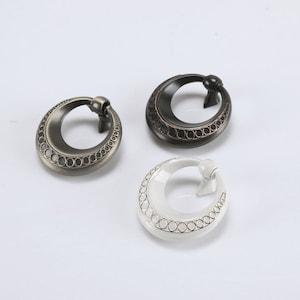 May include: Three decorative cabinet pulls in different finishes: antique brass, bronze, and white. Each pull is a round ring with a decorative border of small circles.