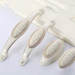 May include: Four white ceramic cabinet door pulls with a gold trim and a crackled finish.