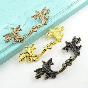 May include: Three ornate drawer pulls with a decorative floral design. The pulls are made of metal and come in gold, brass, and black finishes.