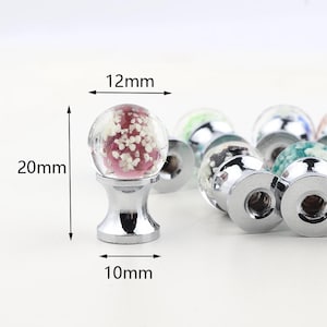 May include: A set of decorative cabinet knobs with a round glass top and a silver base. The glass tops have a variety of colors and patterns, including pink with white flecks. The knobs measure 12mm in diameter, 20mm in height, and 10mm in base diameter.