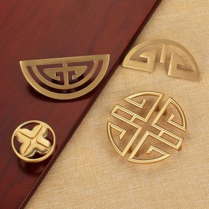 May include: Four gold-toned cabinet knobs with intricate geometric designs. The knobs feature a variety of patterns, including circles, squares, and triangles.