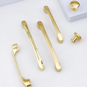 May include: Five gold cabinet knobs and pulls, including a round knob, a small knob, and three different styles of pulls.