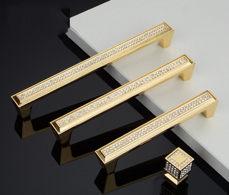 May include: Three gold cabinet pulls with a row of clear rhinestones. A matching gold knob with rhinestones is also shown.