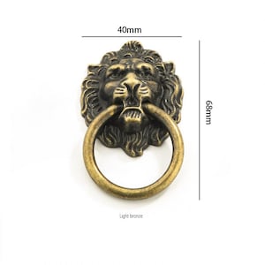 May include: A light bronze lion head ring pull with a 40mm diameter and 68mm height. The ring pull is a decorative hardware piece for furniture or cabinets.