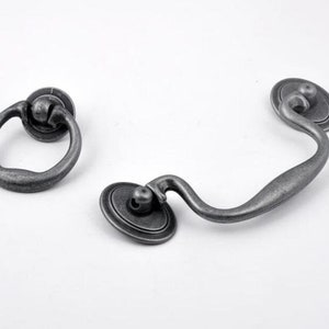 May include: Two antique silver drawer pulls. One is a ring pull and the other is a curved pull with a rounded end.