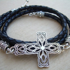 May include: A black leather braided bracelet with a silver ornate cross pendant. The bracelet has two silver bead accents.