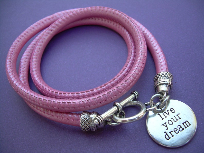 Op de afbeelding: Een roze leren armband met een zilveren bedel met de tekst "live your dream".