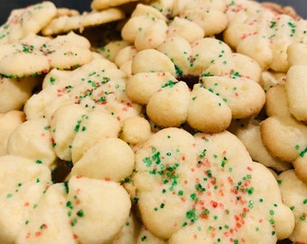 May include: Close-up of a pile of flower-shaped cookies with green and red sprinkles. The cookies are a light golden color and appear to be freshly baked. The image is well-lit, showcasing the texture and details of the treats.