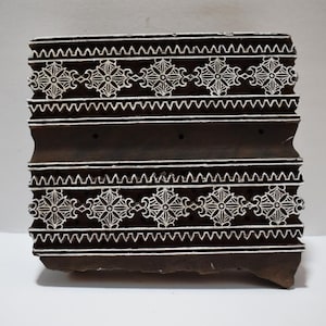 May include: A wooden printing block with a carved design of repeating white floral patterns on a dark brown background.