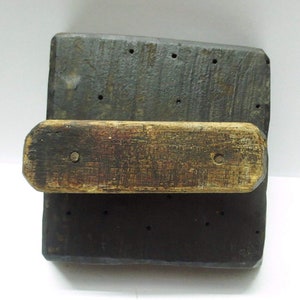May include: A wooden printing block with a handle. The block is dark brown and has a series of holes drilled into it. The handle is made of lighter wood and is attached to the block.