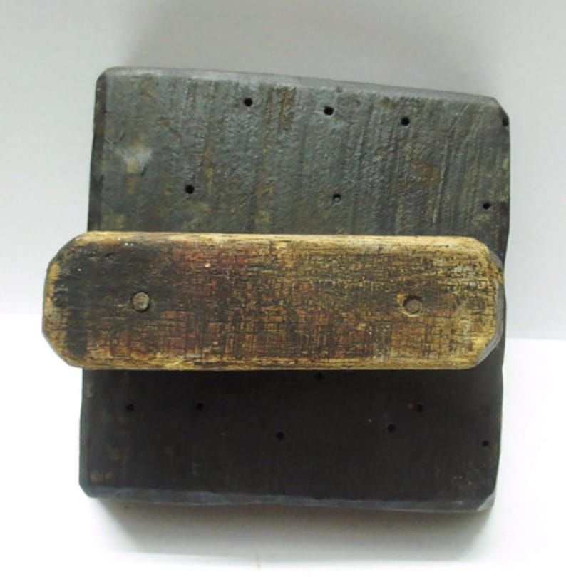 May include: A wooden printing block with a handle. The block is dark brown and has a series of holes drilled into it. The handle is made of lighter wood and is attached to the block.