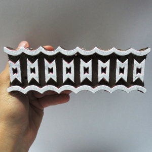 May include: A brown wooden block printing stamp with a white design of repeating geometric shapes. The stamp has a scalloped edge.