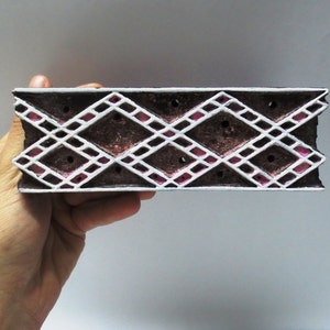 May include: A wooden printing block with a white and pink geometric design. The block is rectangular and made of dark brown wood.