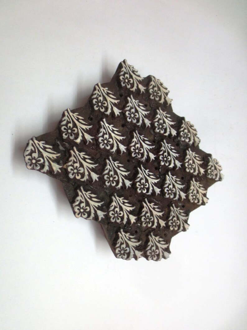 Pode incluir: Um bloco de impress&atilde;o de madeira com um design floral. O bloco &eacute; esculpido com um padr&atilde;o repetitivo de flores brancas e folhas sobre um fundo marrom escuro.