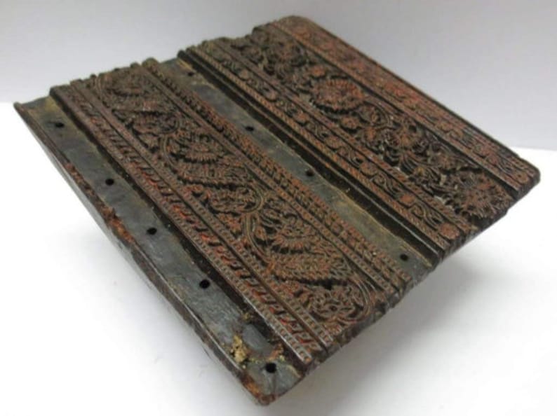 May include: A wooden printing block with intricate floral designs carved into the surface. The block is dark brown and has a worn, aged appearance.