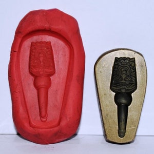 May include: Two molds for making a decorative object. One mold is red rubber and the other is a metal mold. Both molds have a design of a torch with a stylized flame and a figure in the center.