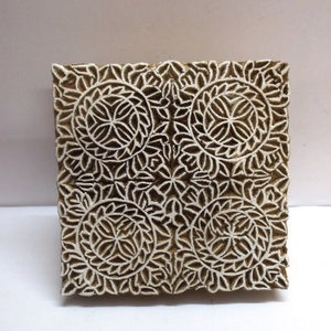May include: A square wooden block printing stamp with a detailed floral design. The design features four repeating circular patterns with intricate details.