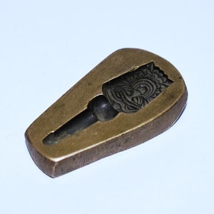 May include: A vintage brass mold for making a decorative object. The mold features a detailed design of a face with intricate patterns.