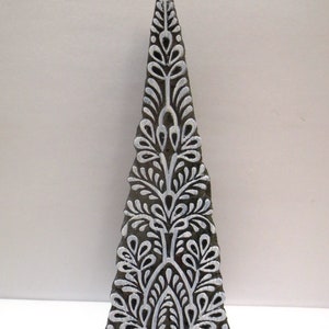 Könnte beinhalten: Ein Holzblock-Stempel mit einem weißen floralen Design in Form eines Dreiecks. Das Design weist komplizierte Details und ein symmetrisches Muster auf.