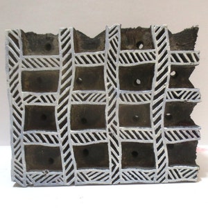 May include: A wooden printing block with a grid pattern carved into the surface. The grid is made up of white lines and has a series of holes in the center of each square.