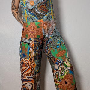 May include: A patchwork jumpsuit with a variety of colorful patterns, including paisley, geometric shapes, and abstract designs. The jumpsuit features adjustable black straps, a large front pocket with a wooden button, and multiple smaller pockets. The overall style is bohemian and artistic.