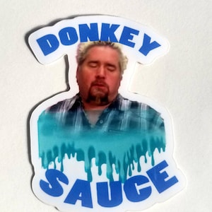 Puede incluir: Una pegatina blanca con un borde azul y el texto "DONKEY SAUCE" en azul. Se ve la cara de un hombre en el centro de la pegatina, con un efecto de goteo azul y verde debajo.