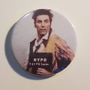 Könnte beinhalten: Ein runder Knopf mit einem Schwarzweiß-Fahndungsfoto eines Mannes mit dunklen Haaren und einem Schnurrbart. Das Fahndungsfoto trägt den Text "NYPD" und die Zahlen "33178 10404". Der Mann trägt ein weißes Hemd und eine gelb-braune gemusterte Weste.