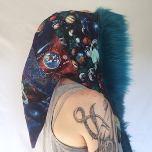 May include: A teal faux fur hooded scarf with a space-themed fabric lining. The fabric features planets, stars, and the words "Earth", "Moon", and "Mars".