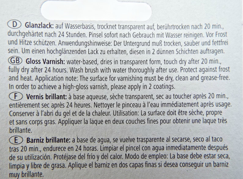 Puede incluir: Primer plano de una etiqueta blanca con texto en varios idiomas, incluyendo ingl&eacute;s, alem&aacute;n, franc&eacute;s y espa&ntilde;ol. El texto describe un barniz transparente a base de agua, que se seca en 20 minutos.