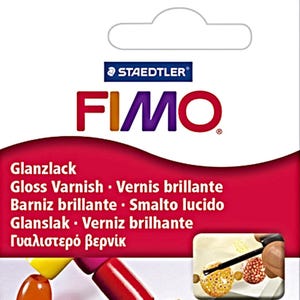 Puede incluir: Un paquete de barniz brillante Staedtler FIMO. El embalaje es blanco con un dise&ntilde;o curvo rojo y morado. El texto "FIMO" est&aacute; en letras grandes y coloridas. El paquete tambi&eacute;n enumera el barniz en varios idiomas.