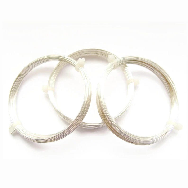 Puede incluir: Tres bobinas circulares de alambre fino de color plateado brillante. Cada bobina est&aacute; asegurada con peque&ntilde;as bridas de pl&aacute;stico blanco para mantener su forma redonda. El alambre tiene un acabado met&aacute;lico liso y est&aacute; dispuesto en superposici&oacute;n.