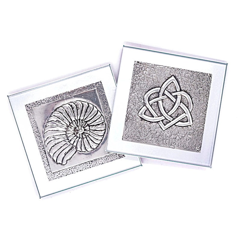 May include: Two silver metal coasters with raised designs. One coaster features a nautilus shell and the other features a Celtic knot.