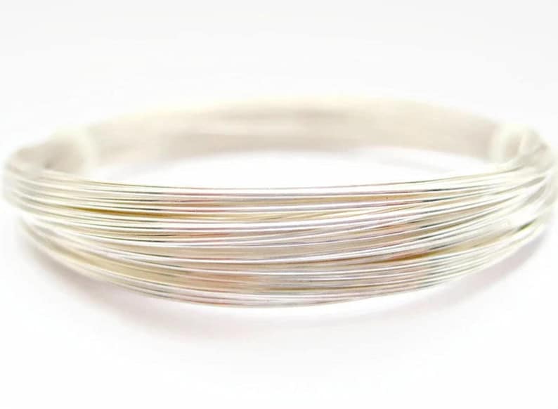 Puede incluir: Una pulsera tipo brazalete de plata de m&uacute;ltiples hilos compuesta por varios alambres met&aacute;licos finos y lisos enrollados juntos para formar una banda circular &uacute;nica con una superficie pulida y reflectante que capta la luz en su estructura uniforme.