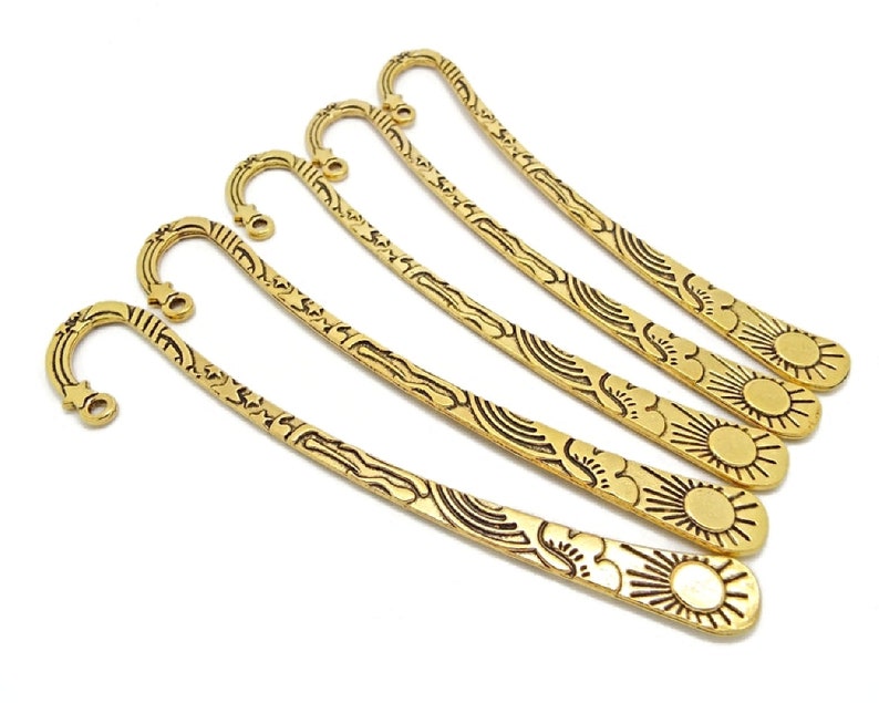 5 gold coloured metal bookmarks in the shape of a shepherds crook with a loop at the top end where beads and charms can be added for decoration.  The bookmark design includes a sun image at the bottom and stars elsewhere.