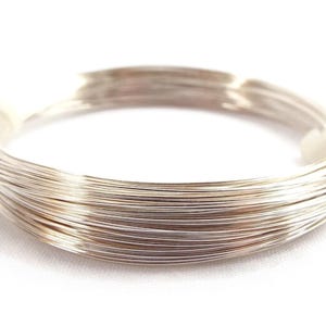 Peut inclure: Une bobine de fil de couleur argent, &eacute;troitement enroul&eacute;e et fix&eacute;e avec une bande blanche. Le fil semble fin et souple, adapt&eacute; &agrave; la fabrication de bijoux ou &agrave; l'artisanat. L'image est sur fond blanc.