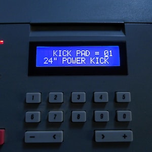 Puede incluir: Primer plano de un dispositivo gris de producción de música electrónica. La pantalla azul muestra "KICK PAD = 01" y "24" POWER KICK." Hay varios botones y controles, incluido un botón "RECORD".
