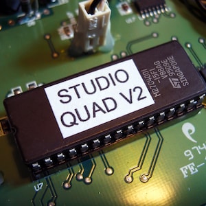 Puede incluir: Primer plano de una placa de circuito impreso negra con un chip gris etiquetado como "STUDIO QUAD V2" y el texto "M27C4001 -15F1 V88AG 9509E SINGAPORE".
