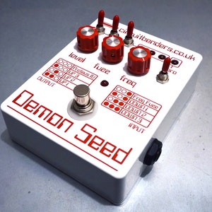 Può includere: Pedale per effetti bianco con scritte e manopole rosse. Il pedale è etichettato "Demon Seed" e ha controlli per "level", "fuzz" e "freq".