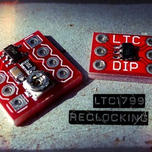 Può includere: Due circuiti elettronici rossi con componenti argentati e il testo "LTC DIP" e "LTC1799 RECLOCKING". Le schede sono quadrate e rettangolari, con più fori circolari argentati.