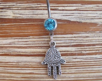 May include: A silver belly button ring with a blue gem and a silver charm in the shape of a hamsa hand.