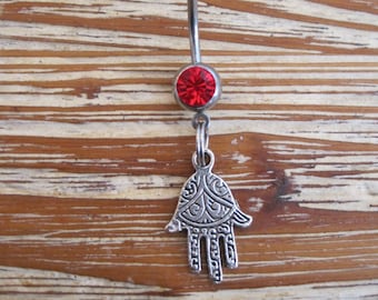May include: Silver belly button ring with a red gem and a silver charm in the shape of a hamsa hand.